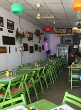 This image shows the cozy interior of Poo Restaurant, featuring a mix of traditional Thai decor and casual seating arrangements. The vibrant dishes on the table showcase a variety of Thai and international cuisines, including crispy prawns and Panang curry. Dim lighting adds warmth to the ambiance, making it a welcoming space for guests. The comfortable environment and delicious food make this restaurant a must-visit for food enthusiasts in Sukhothai.