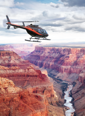 This image shows a breathtaking aerial view of the Grand Canyon from a helicopter tour. Passengers soar above the canyon’s vast expanse, witnessing the magnificent rock formations and the winding Colorado River below. A helicopter tour offers a unique perspective of the canyon that few visitors ever get to experience. The bird’s-eye view captures the grandeur of the canyon, providing a thrilling adventure that showcases the true scale and beauty of this natural wonder.