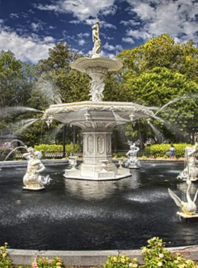 This image shows the stunning Forsyth Fountain at the north end of Forsyth Park in Savannah, Georgia. It captures the beauty of the iconic fountain surrounded by lush greenery and walking paths. People can be seen strolling through the park, enjoying the peaceful environment. The fountain is a perfect example of the city's rich history and serene atmosphere, making it a popular spot for relaxation and photos.