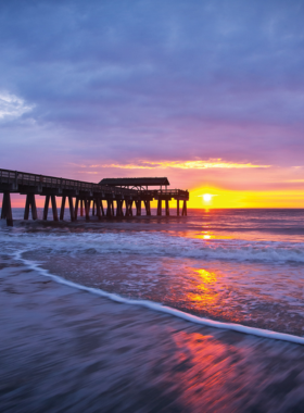 This image shows the pristine sandy beaches of Tybee Island, located just outside of Savannah, Georgia. The scene captures beachgoers relaxing under the sun, while others enjoy swimming or walking along the shore. The calm waves and clear water make it a perfect spot to unwind and escape the hustle of the city. Tybee Island is a popular beach destination known for its peaceful atmosphere, natural beauty, and laid-back vibe.