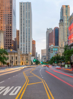  This image shows the vibrant and bustling Magnificent Mile in Chicago, a famous shopping and sightseeing destination. The street is lined with high-end boutiques, department stores, and luxury brands, with people walking along the sidewalks. Iconic landmarks like the Wrigley Building and Tribune Tower stand tall in the background. The lights from shops and street lamps create a lively and energetic atmosphere. The street performers and tourists add to the lively experience, making it a must-visit spot for anyone exploring the city.