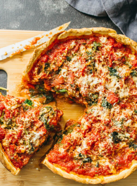 This image shows a delicious deep-dish pizza, a specialty of Chicago, with a thick, buttery crust, layers of melted cheese, and rich tomato sauce on top. A slice is being lifted, revealing the gooey cheese stretching from the pizza pan. The crust is golden brown, and the toppings, such as sausage and vegetables, make it look even more appetizing. The restaurant setting adds to the experience, with a cozy ambiance and a plate of pizza in focus, making it a mouth-watering sight for food lovers.