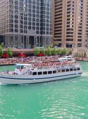 This image shows a scenic view of Chicago’s skyline from an architecture river cruise. A tour boat is floating on the Chicago River, surrounded by towering skyscrapers like the Willis Tower and Tribune Tower. The clear blue sky reflects on the water, creating a beautiful contrast. People on the boat are taking photos and listening to the guide as they learn about the history of the city’s iconic buildings. The view captures the essence of Chicago’s impressive architecture and offers a relaxing sightseeing experience.