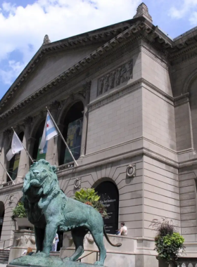 This image shows the grand entrance of the Art Institute of Chicago, a world-renowned museum. The historic building has large stone lion statues at the front, welcoming visitors. The entrance is busy with art lovers, students, and tourists walking in and out. Inside, famous paintings such as Van Gogh’s The Bedroom and Grant Wood’s American Gothic are displayed on the walls. The museum’s modern wing, filled with natural light, showcases contemporary art, making it a must-visit for anyone interested in culture and creativity.