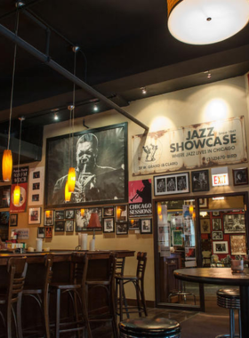 This image shows a lively jazz and blues performance at a famous Chicago club. The dimly lit stage has musicians playing instruments like the saxophone, piano, and drums, creating a soulful ambiance. The audience is seated at cozy tables, enjoying drinks while listening to the rhythmic tunes. The club’s old-school charm, with wooden interiors and vintage decorations, adds to the experience. A neon sign reading "Live Jazz & Blues" glows in the background, making it a perfect scene for music lovers.