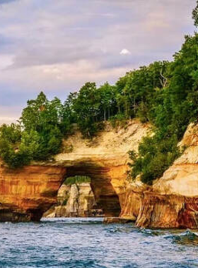 This image shows the majestic Arch Rock, a natural limestone formation located on Mackinac Island. Arch Rock rises 146 feet above the ground and provides a stunning view of the island's surroundings. Visitors can either hike or take a carriage ride to reach the top, where they can enjoy breathtaking views of the lush landscape and Lake Huron. The geological wonder is a must-see for anyone visiting the island, offering a blend of natural beauty and adventure.