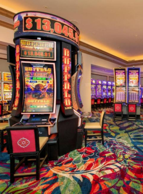 This image shows the vibrant exterior of the Beau Rivage Casino at night, illuminated by bright golden lights. The entrance is grand, with a large fountain in front reflecting the dazzling lights. Inside, a casino floor is filled with lively slot machines, poker tables, and excited guests enjoying the thrilling atmosphere. Some visitors are sipping cocktails at a stylish lounge, while others enjoy fine dining with beautifully plated seafood dishes. The luxurious and high-energy setting makes it a must-visit spot in Biloxi.