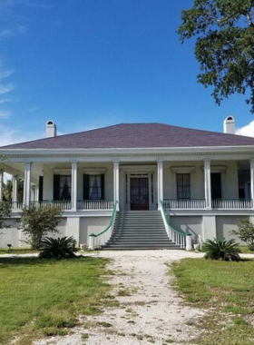 This image shows the Beauvoir mansion, a beautifully preserved historical home surrounded by green lawns and large oak trees. The white columns and classic Southern architecture give it an elegant look. Visitors are walking up the steps, while a tour guide explains the historical significance of Jefferson Davis's former home. Inside, antique furniture and Civil War-era artifacts are displayed, offering a glimpse into the past. The peaceful coastal setting adds to the charm of this historic landmark.