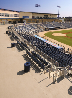 This image shows a baseball game at MGM Park, with a lively crowd cheering. The field is bright green, and the Gulf Coast skyline is visible in the background. Fans enjoy classic stadium snacks like popcorn and nachos.