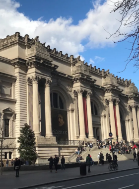 This image shows the grand entrance of The Metropolitan Museum of Art, one of the world’s most famous museums. The historic building features impressive architecture with tall columns and large windows. Visitors gather on the wide stone steps, some taking photos while others relax before entering. Inside, the museum houses breathtaking artworks, including ancient Egyptian artifacts, European masterpieces, and modern sculptures, making it a paradise for art lovers.