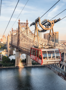 This image shows the Roosevelt Island Tram gliding above the East River, providing an aerial view of Manhattan’s skyscrapers and the Queensboro Bridge. The bright red cable car carries passengers high above the water, offering breathtaking panoramic views of the city. The ride is smooth, affordable, and perfect for those looking to experience New York from a unique perspective.