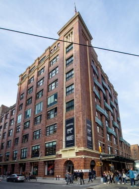 This image shows the vibrant Chelsea Market, an indoor food hall filled with a variety of delicious dishes. People are seen enjoying fresh seafood, tacos, and gourmet desserts at stylish food stalls. The industrial-style architecture, with exposed brick walls and vintage lighting, adds charm to the space. Visitors explore boutique shops and art displays, making Chelsea Market a perfect blend of food, culture, and creativity.