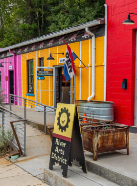 This image shows a lively scene at Asheville’s River Arts District, where colorful murals decorate brick buildings, and local artists showcase their work in open studios. The industrial-style warehouses have been transformed into vibrant creative spaces filled with paintings, pottery, and handmade crafts. Visitors can be seen walking along the streets, exploring galleries, and enjoying street art in this artistic community.