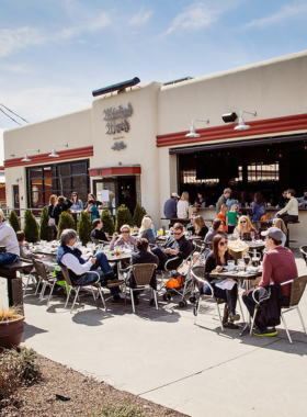 This image shows the lively atmosphere inside Wicked Weed Brewing Pub, where people are gathered around wooden tables enjoying craft beers. The interior features exposed brick walls, rustic wooden décor, and hanging Edison lights. Behind the bar, large brewing tanks are visible, showcasing the brewery’s commitment to high-quality, innovative beer-making. The warm and inviting setting makes it a popular hangout spot.