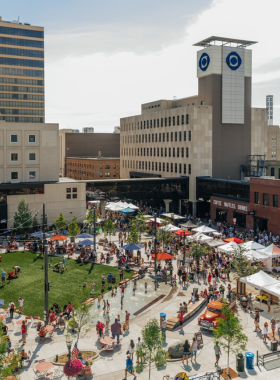 This image shows the Red River Market, Fargo’s largest and most vibrant farmers’ market, bustling with people shopping for fresh fruits, vegetables, baked goods, and artisan crafts. Local vendors have set up colorful stalls, offering handmade products, organic honey, and farm-fresh flowers. Visitors are seen sipping locally roasted coffee and enjoying live music performances by street musicians. The market is an outdoor community hub where families, friends, and tourists gather to experience Fargo’s local culture, friendly atmosphere, and delicious food in a lively setting.