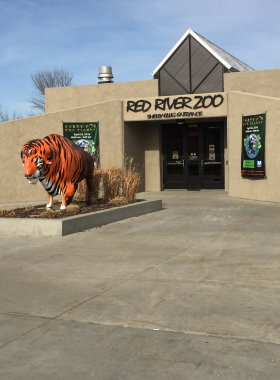 This image shows the Red River Zoo in Fargo, North Dakota, featuring beautiful walking paths, lush greenery, and animal enclosures. The zoo is known for its cold-climate species, including red pandas, gray wolves, and Pallas’ cats. Visitors can be seen enjoying the exhibits, learning about conservation efforts, and taking photos of exotic wildlife. The zoo has an interactive farm area, making it a great place for families and kids to experience nature and animals up close in a well-maintained environment.