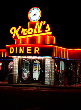 This image shows a delicious serving of hotdish, a classic Midwestern comfort food, at Kroll’s Diner in Fargo. The dish features a baked casserole with creamy potatoes, melted cheese, and seasoned ground beef. The restaurant’s retro 1950s diner interior is visible in the background, with checkered floors and cozy booths. Customers are enjoying their meals, making it a perfect place for food lovers to experience Fargo’s local flavors.