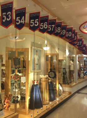 This image shows the Roger Maris Museum, a tribute to the legendary baseball player, located inside West Acres Mall in Fargo. The museum features memorabilia, photographs, and a replica of Maris’s Yankees locker. Baseball fans are reading about his achievements and watching documentary clips. The exhibit is small yet meaningful, offering an insight into Maris’s record-breaking career and his ties to Fargo’s sports history.