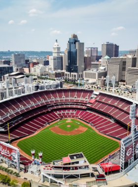 This image shows the Great American Ball Park, the home of the Cincinnati Reds, packed with enthusiastic baseball fans. The stadium features breathtaking riverfront views, bright stadium lights, and a massive scoreboard displaying the game. Fans in red jerseys cheer as a player hits a home run, and the crowd erupts with excitement. Classic baseball snacks like hot dogs, popcorn, and nachos are seen in the hands of spectators. The image captures the thrilling atmosphere of a live game, with players in action, families enjoying the experience, and the spirit of America’s favorite pastime filling the air.