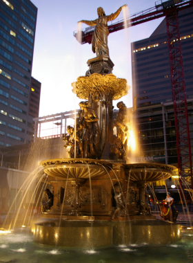 This image shows Fountain Square, the lively heart of downtown Cincinnati, bustling with people around the iconic Tyler Davidson Fountain. The plaza is surrounded by tall buildings, restaurants, and cafés. A group of friends enjoys coffee at an outdoor seating area while others watch a live performance on the stage. In winter, the square transforms into an ice-skating rink with twinkling holiday lights. The vibrant energy of the place, whether during food festivals, summer movie nights, or daily gatherings, makes it a must-visit spot for both locals and tourists.