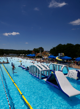 This image shows Coney Island Park, a lively amusement and water park with thrilling water slides, a massive wave pool, and classic rides. Families and thrill-seekers can be seen floating on the lazy river, enjoying the high-speed water attractions, or relaxing in the sun. Brightly colored rides and cheerful parkgoers create a vibrant atmosphere, making it a favorite summer destination. The park’s long history, spanning over 130 years, is reflected in its nostalgic charm, with traditional carnival games, live shows, and fun-filled activities for visitors of all ages.