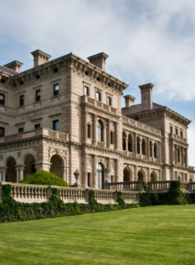 This image shows the grand exterior of The Breakers Mansion in Newport, Rhode Island, a famous Gilded Age mansion built by the Vanderbilt family. The mansion features intricate architectural details, large columns, and a stunning ocean view in the background. The golden chandeliers and elegant marble interiors make it one of the most luxurious historic homes in the U.S. The mansion attracts history lovers and tourists who admire its rich heritage and design.

