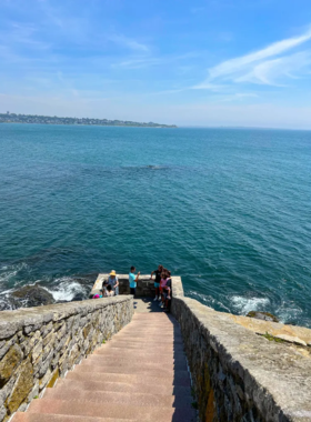 This image shows Newport’s famous Cliff Walk, a scenic 3.5-mile trail that runs along the rocky coastline with breathtaking ocean views. The walkway is lined with lush greenery on one side and historic mansions on the other. The waves crash against the cliffs below, creating a stunning natural backdrop. The path is popular among photographers, joggers, and tourists who come to enjoy the fresh air and picturesque scenery.