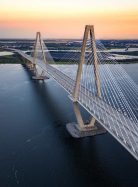 This image shows the Arthur Ravenel Jr. Bridge in Charleston, a modern engineering marvel that connects downtown Charleston to Mount Pleasant. The bridge’s sleek cables and towers stand tall against the backdrop of the Cooper River. The view from the bridge offers panoramic vistas of the city, the harbor, and nearby islands. The image also features a person walking along the pedestrian path, showing that visitors can enjoy a scenic walk or bike ride across the bridge, taking in the views.