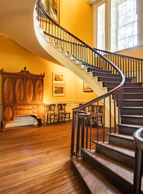 This image shows the Nathaniel Russell House in Charleston, an 1808 Federal-style mansion known for its architectural beauty. The image highlights the iconic floating staircase and grand rooms inside the house, where visitors can experience the elegance of Charleston’s elite. The historical house is surrounded by lush greenery, offering a glimpse into the past. The house provides an intimate look into Charleston's aristocratic lifestyle during the early 19th century, showcasing its refined interiors and rich history.