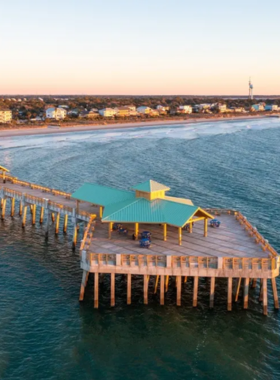 This image shows Folly Beach, a popular coastal destination near Charleston. The image features a serene beach with golden sand, gentle waves, and a vibrant sunset in the background. Visitors are seen relaxing on the beach, soaking up the sun, and enjoying the peaceful atmosphere. The beach is an ideal spot for swimming, surfing, and watching wildlife, with the stunning natural scenery providing a perfect place to unwind and enjoy Charleston's beautiful coastline.