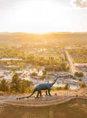 This image shows a large green dinosaur sculpture at Dinosaur Park in Rapid City, standing tall on a hilltop against a bright blue sky. The dinosaur statues are playful and colorful, designed for kids and families to climb on and explore. The park also provides a panoramic view of the city, with scenic trails leading to different dinosaur exhibits. Tourists and families can be seen taking photos and enjoying the unique, historic roadside attraction, which has been a favorite spot since the 1930s.