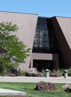 This image shows an indoor exhibit at the Journey Museum and Learning Center in Rapid City, featuring Native American artifacts, fossils, and interactive displays. Visitors, including families and history enthusiasts, are engaged in learning about the geological and cultural history of the Black Hills. Glass cases hold ancient tools, pottery, and gold mining relics from the past. The lighting is dim, focusing on the historical items that tell the story of the region’s evolution, including Native American heritage, early settlers, and scientific discoveries.