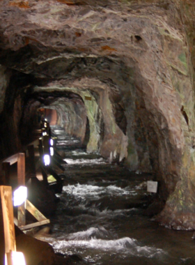 This image shows the breathtaking underground formations of Black Hills Caverns, featuring stalactites hanging from the cave ceiling and stalagmites rising from the ground. A guided tour is taking place, with visitors walking along a well-lit pathway, admiring the natural rock formations created over millions of years. The cave’s walls glisten under the soft lights, highlighting the intricate textures and mineral deposits. The underground environment is cool and mysterious, offering a fascinating exploration experience.