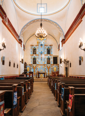 This image shows the impressive stone architecture of Mission San Jose, also known as the “Queen of the Missions.” The massive church with intricate carvings stands proudly under a bright blue sky, surrounded by historic courtyards. Visitors walk through the ancient archways, admiring the beautifully preserved walls and learning about the mission’s deep historical and cultural significance in Texas' Spanish colonial history.