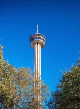 This image shows the breathtaking view from the Tower of the Americas, overlooking the sparkling skyline of San Antonio. The observation deck provides a stunning 360-degree panorama of the city, with famous landmarks visible in the distance. Visitors stand by the glass windows, taking in the incredible sights, while the rotating Chart House restaurant offers a luxurious dining experience with unmatched views.