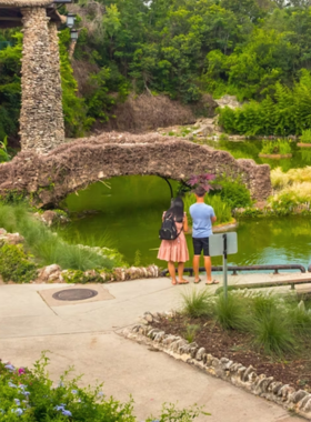 This image shows the lush greenery of Brackenridge Park, with families enjoying a picnic under tall oak trees. A small train is seen winding through the scenic trails, offering rides to children and adults. The peaceful surroundings include a river, walking paths, and access to the San Antonio Zoo, making it an ideal location for relaxation and outdoor fun.