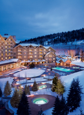 This image shows the luxurious Deer Valley Resort with its well-groomed ski slopes and skiers enjoying the winter wonderland. The image captures the elegance and exclusivity of the resort, which is known for its skier-only policy. Snow-covered mountains stretch across the horizon, while a beautifully designed lodge with wooden accents stands at the base. Some visitors are seen sipping hot drinks on an outdoor terrace, enjoying the view. The perfectly carved ski trails are lined with tall pine trees, adding to the charm. The resort's world-class amenities, including high-end accommodations and gourmet dining, make it a top choice for ski enthusiasts. The bright sun reflects off the snow, creating a dazzling effect. A skier in motion glides down the slope, leaving a trail of fresh powder behind. This image perfectly captures the mix of adventure and luxury that defines Deer Valley Resort.