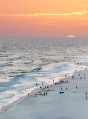 This image shows the vibrant and bustling Wharf at Orange Beach, with the iconic Ferris wheel towering above the area. The Wharf is full of activity, offering shopping, dining, and entertainment options. The evening sky is lit up with the SPECTRA laser light show, adding to the excitement. People are seen enjoying the view from the Ferris wheel, shopping at boutique stores, and dining at waterfront restaurants, capturing the lively atmosphere of this entertainment hub.