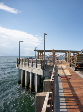 This image shows the Gulf State Park Pier stretching into the Gulf of Mexico, providing stunning ocean views at sunset. Anglers can be seen casting their lines into the water, while others stroll along the pier, enjoying the peaceful evening. The golden hour casts a warm glow over the water, creating a serene and picturesque scene. The image captures the beauty of the pier and its perfect setting for relaxation and fishing.