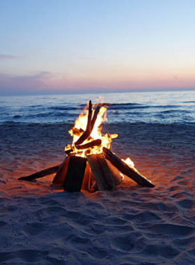 This image shows a cozy beach bonfire in Gulf Shores at night, with people sitting around the fire, roasting marshmallows, and enjoying the warm glow. The starry sky and the sound of waves crashing create a peaceful, magical atmosphere. The image highlights the warmth and camaraderie of this evening activity, capturing the essence of a relaxing and memorable experience by the beach.